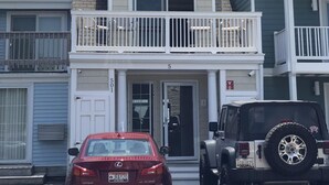 Un immeuble de deux étages doté d’un balcon, d’un garage et d’une allée menant à un emplacement où sont garées une voiture rouge et un VUS blanc.