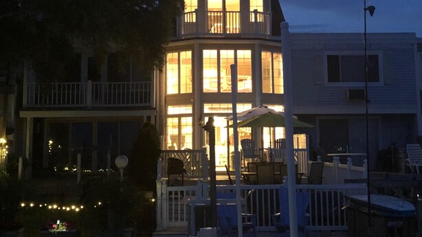 Une maison située au bord de l’eau, dotée d’un balcon, d’une véranda et d’un intérieur bien éclairé.