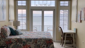 Une chambre dotée d’un grand lit, d’un bureau et offrant une vue sur l’eau grâce à de grandes fenêtres.