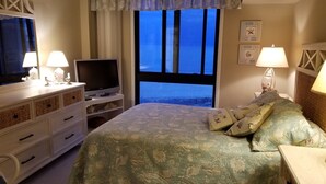 Una camera da letto con un letto, una cassettiera, un televisore e vista sul mare dalla finestra.