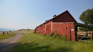 A red barn with a dirt path leading to it, surrounded by green grass and a wooden fence.