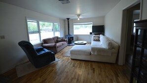 A spacious living room with hardwood flooring, a large white sofa, a smaller sofa, a blue chair, and a flat-screen TV.