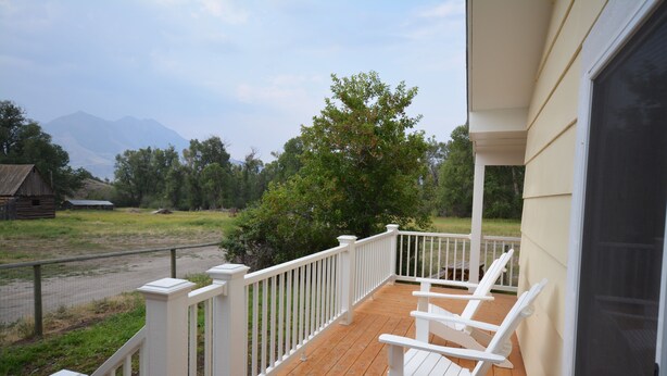 A wooden deck with white railings and chairs, overlooking a grassy area with trees and a mountain in the distance.