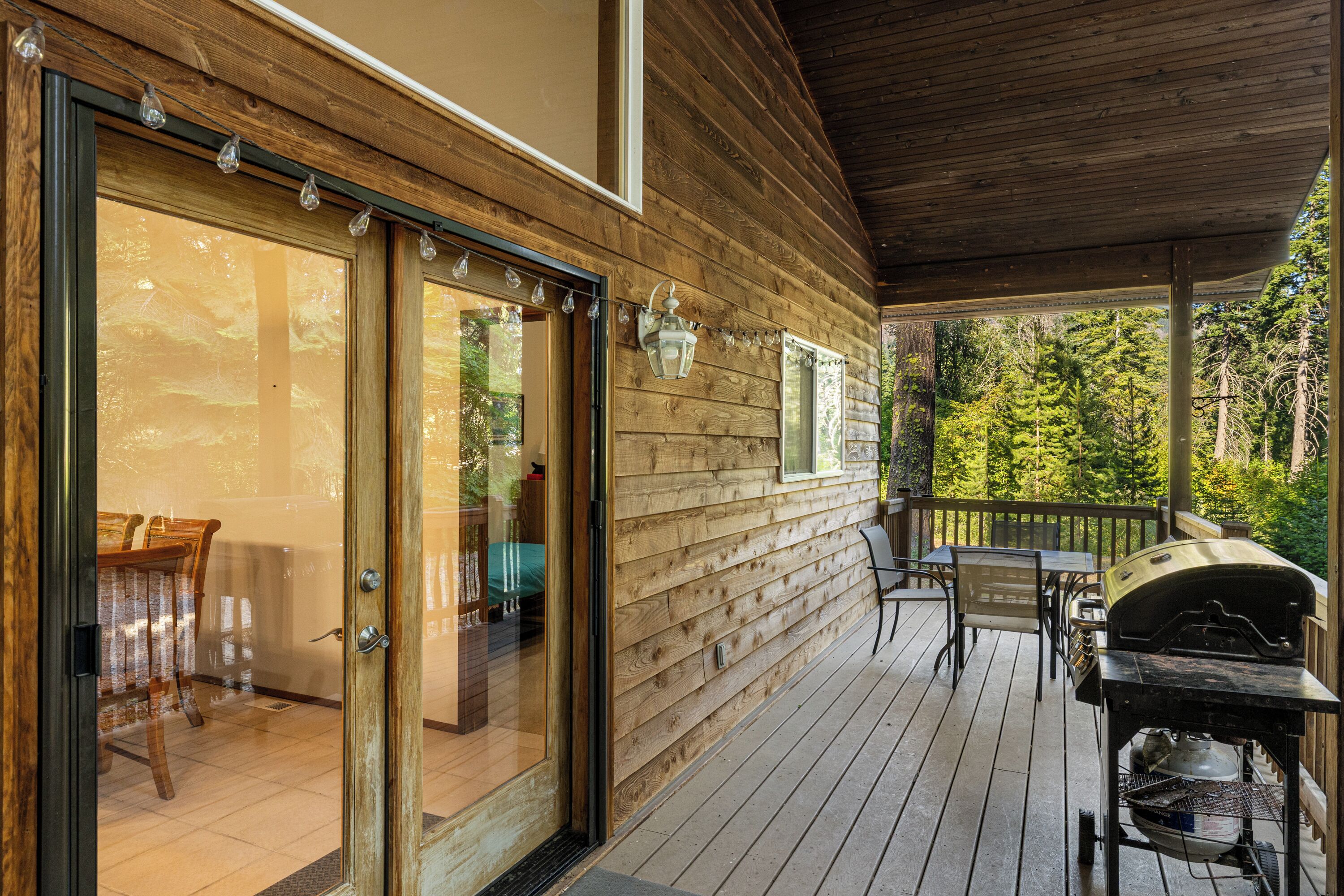 A wooden deck with a glass door leading to a room, outdoor furniture, and a barbecue grill.