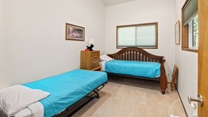 A bedroom with two single beds, a wooden dresser, a nightstand, a lamp, a framed picture, and a window with blinds. - Elk Tracks Lodge (Easton)
