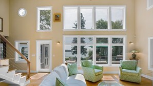 Un ampio soggiorno con soffitto alto, ampie finestre, una scala e arredi decorati con motivi verdi.