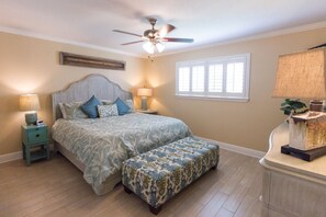 Une chambre à coucher comprenant un lit, des tables de chevet, un ventilateur de plafond, une fenêtre et une petite table de nuit.