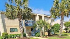 A building with a parking lot, palm trees, and a blue staircase. - Happy Place Chateau La Mer II #1301 2-Bd 2-Bth Ground Floor Private Patio (Destin)