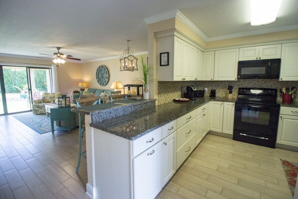 A kitchen with white cabinets, a granite countertop, a black oven, and a microwave.