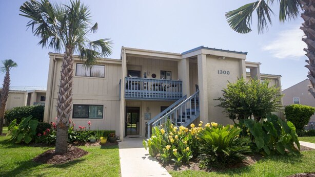 A two-story building with a balcony on the second floor, a visible entrance, and a number '1300' on the facade. - Happy Place Chateau La Mer II #1301 2-Bd 2-Bth Ground Floor Private Patio (Destin)
