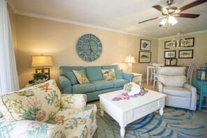 A living room with a sofa, a coffee table, a clock, and a ceiling fan.
