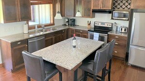 A kitchen with granite countertops, wooden cabinets, stainless steel appliances, and a central island with chairs.