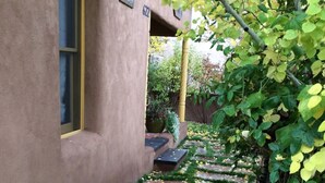 A stone pathway with yellow leaves and green grass, leading to a building with a window and a door.