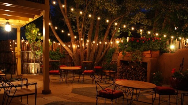 An outdoor patio area with round tables and chairs, string lights, and a wooden fence.
