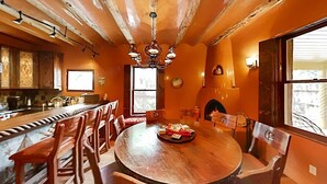 A dining area with a large round table, wooden chairs, a chandelier, and a fireplace.
