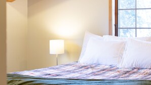 Ein Schlafzimmer mit Holzboden, einem Fenster, einem Bett mit kariertem Überwurf und einer Nachttischlampe.