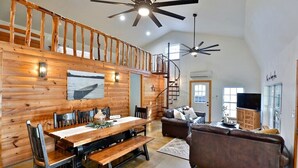 Ein geräumiger Loft mit hohen Decken, Holzwänden, einer Essecke mit langem Tisch und Bänken, einem Ledersofa und einer Treppe zu einer erhöhten Ebene.