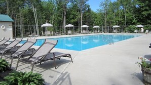 A swimming pool with lounge chairs and umbrellas, surrounded by trees.