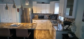 Una cocina moderna con armarios blancos, electrodomésticos de acero inoxidable, encimera de granito y piso de madera.