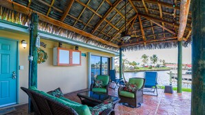 An outdoor patio with wicker furniture, a thatched roof, and a view of a marina.