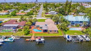 A residential area with a house featuring a swimming pool, docked boats, and a clear view of the surrounding neighborhood.