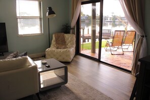 Een woonkamer met een bank, een bijzettafeltje, een lamp en uitzicht op een terras met stoelen en een tafel.