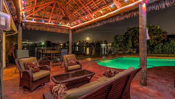 An outdoor patio with wicker furniture, a pool, and a thatched roof structure.