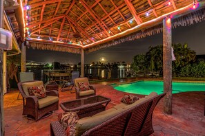 Un patio al aire libre con mobiliario de mimbre, una piscina y una estructura de techo de paja.