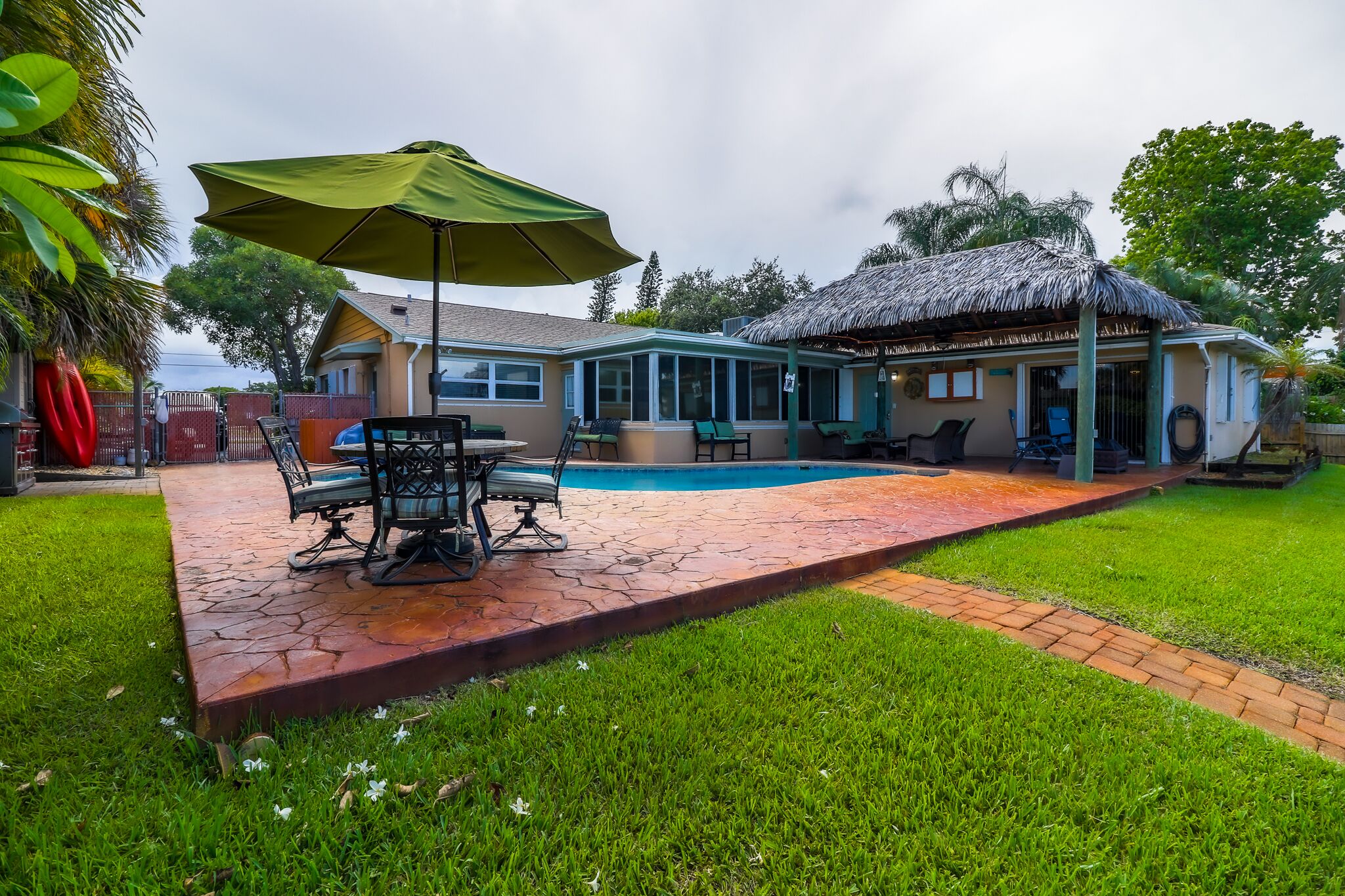 A backyard with a pool, a covered patio, and a thatched-roof structure.