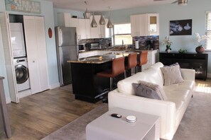 Een knus woongedeelte met een kitchenette, een bank, een salontafel en een wasmachine.