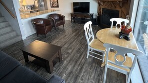 Un salon moderne avec un coin repas, une cuisine à l’arrière-plan, une grande horloge au mur et un ventilateur de plafond.