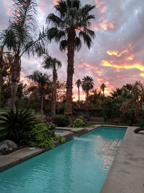 Una piscina con palme e un tramonto sullo sfondo.
