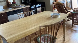 Una mesa de comedor de madera con sillas, un área de cocina con microondas y estufa, y una estantería con libros y objetos decorativos.