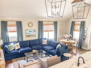 A living room with a blue sofa, a glass coffee table, a dining area with a round table, and a kitchen area with a sink. - Guesthouse Charleston: WEST (64) (Charleston)
