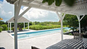 Et poolområde med tag, en pavillon, en pool og en terrasse med bord og stole.