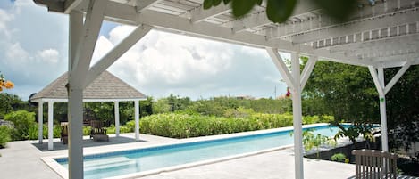Et poolområde med tag, en pavillon, en pool og en terrasse med bord og stole.