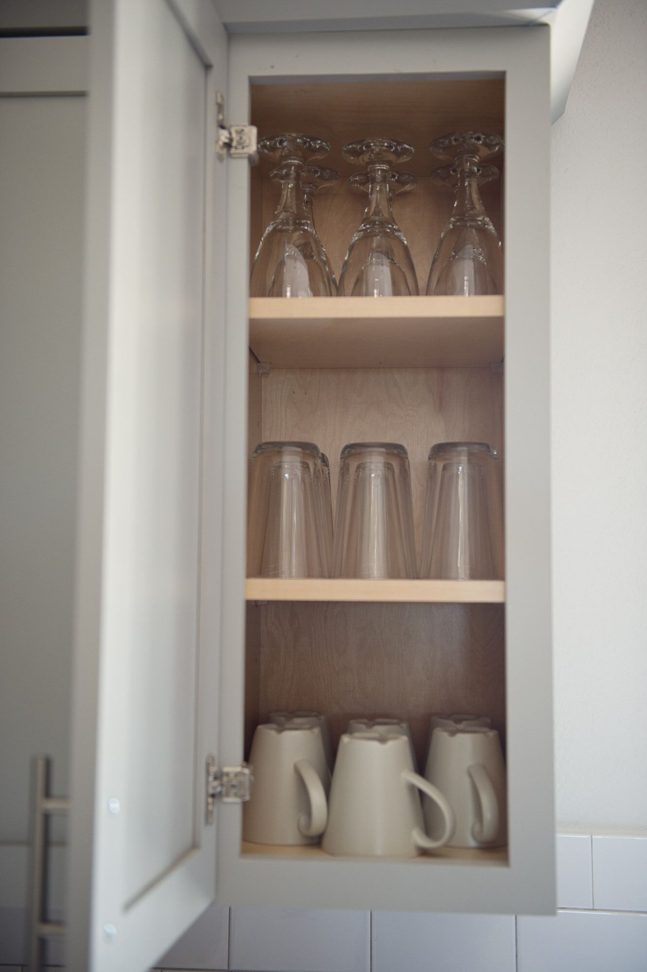 A cabinet with shelves containing glassware and ceramic mugs.