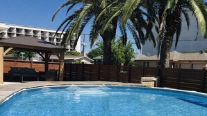 Una piscina con muelle de madera, zona de estar cubierta y valla.