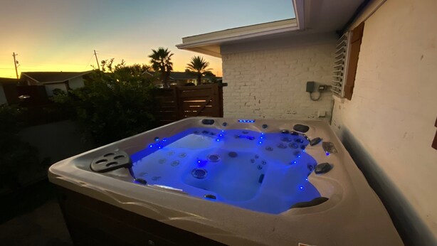 Un jacuzzi con luces LED azules, una pared de ladrillo blanco y una valla de madera al fondo.