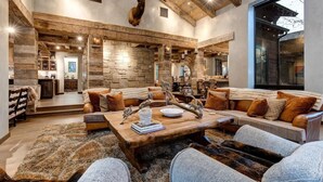 A spacious living area with a stone wall, a mounted elk head, and a large wooden coffee table. - Abode at Three Bears, stunning wilderness estate (Jackson)