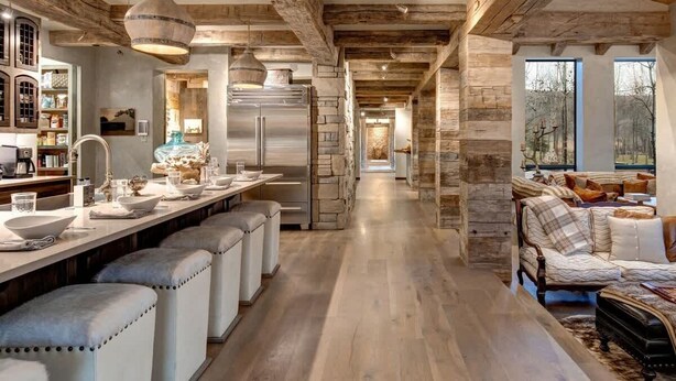 A modern kitchen with a long island, stone walls, and a cozy seating area with a sofa and ottomans. - Abode at Three Bears, stunning wilderness estate (Jackson)