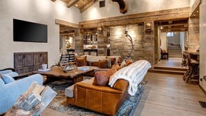 A spacious living area with a stone wall, wooden ceiling beams, and a mounted deer head. - Abode at Three Bears, stunning wilderness estate (Jackson)
