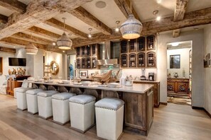 A rustic kitchen with exposed beams, a central island with stools, and a large window. - Abode at Three Bears, stunning wilderness estate (Jackson)