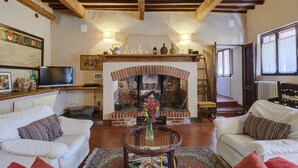 Un salon avec une cheminée, deux canapés blancs, une table basse avec des magazines et un téléviseur posé sur une étagère.