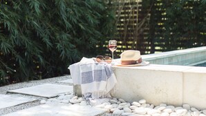 Un cadre extérieur paisible, avec une bordure en béton, une table recouverte d’une nappe blanche, un verre à vin et un chapeau.