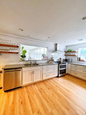 A modern kitchen with white cabinetry, wooden flooring, and a built-in oven. - The Fig House | Mid Century Modern | Minutes from the Beach with a Heated Pool (Saint Simons Island)