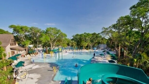 Un parc aquatique doté d’une grande piscine, de toboggans et d’espaces de détente, le tout entouré d’arbres.
