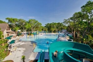 Un parc aquatique doté d’une grande piscine, de toboggans et d’espaces de détente, le tout entouré d’arbres.