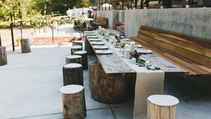 An outdoor dining area with a long wooden table set with white plates, candles, and flowers. There are wooden stools and benches around the table. - Sabor Mexicano Vacation Retreat, (Guerneville)