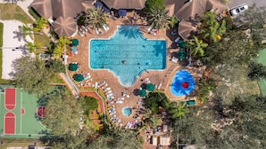Ein Luftbild eines Resorts mit einem zentralen Schwimmbecken, Liegestühlen, Palmen und einem Basketballplatz.